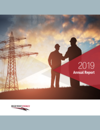 Two individuals in silhouette stand in front of a power line tower at sunset. The image is the cover of the 2019 Annual Report for High West Energy. The HWE logo is visible at the bottom left.